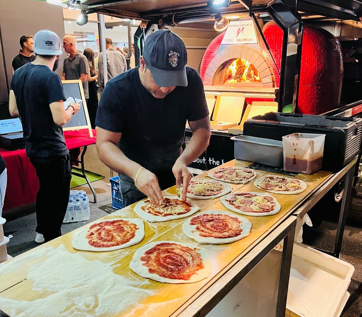 Chef topping pizzas beside the woodfired oven